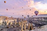 Bunte Heißluftballons über einer großen Felsenformation in Kappadokien
