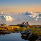 Vier Personen sitzen in der Dämmerung und schauen auf große Eisberspitzen