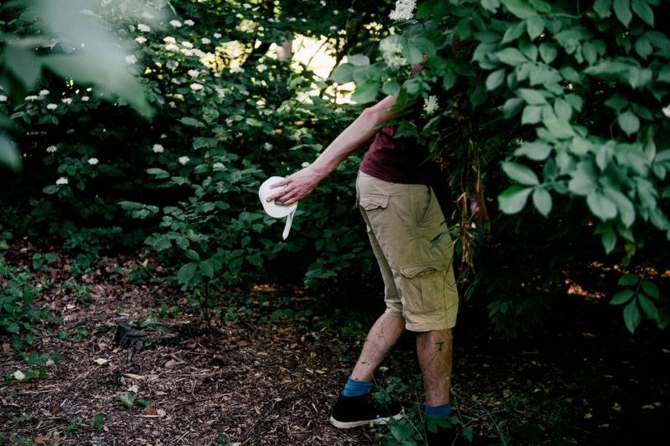 Mann geht mit Toilettenpapier in ein Gebüsch