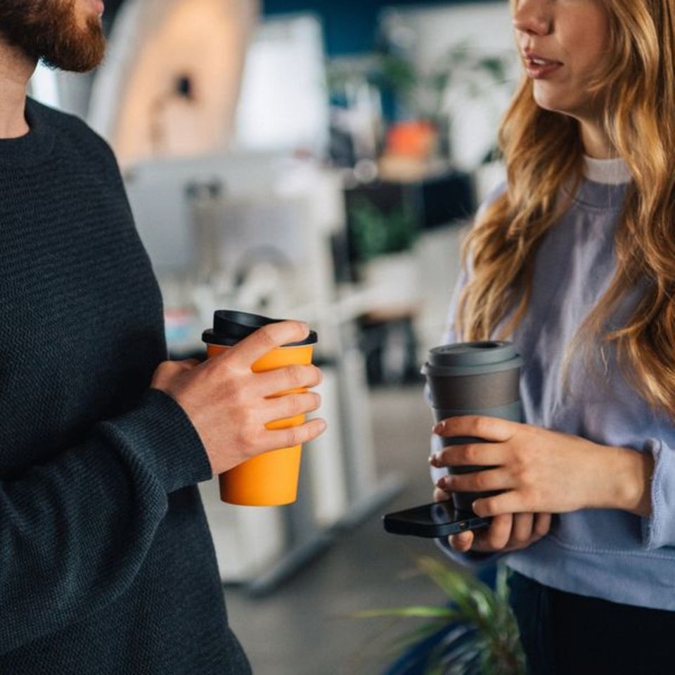 Zwei Menschen mit Kaffeebechern in der Hand