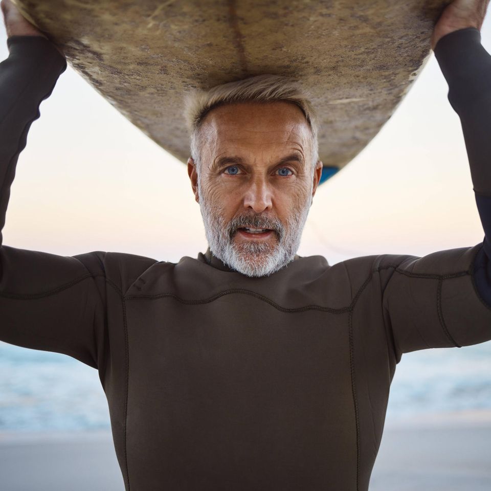 Ein älterer Mann stützt ein Surfbrett mit dem Kopf