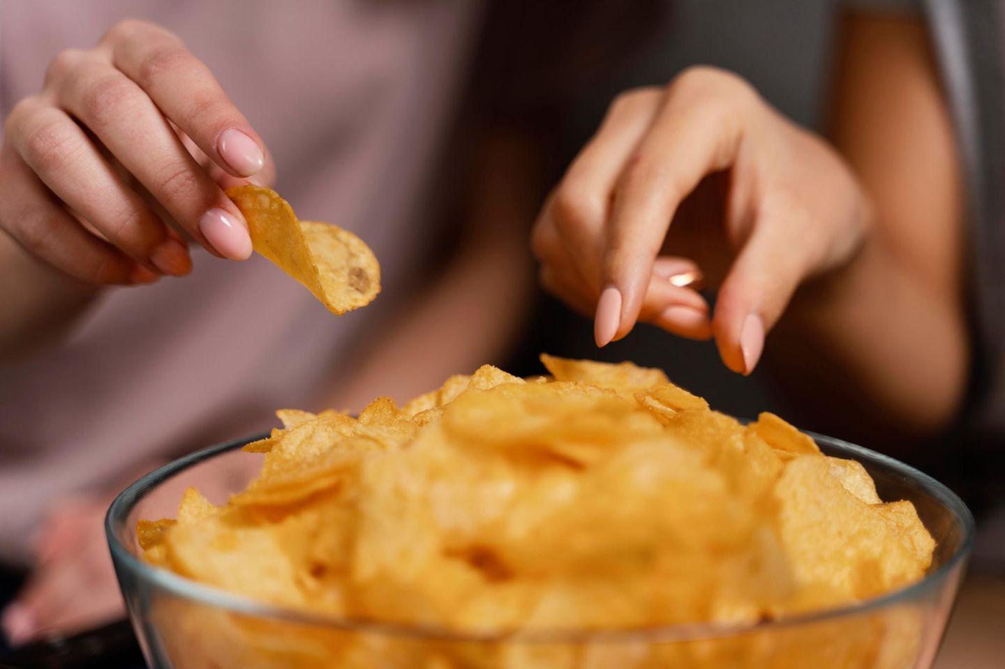 Eine weibliche Hand greift in eien Schale mit Chips