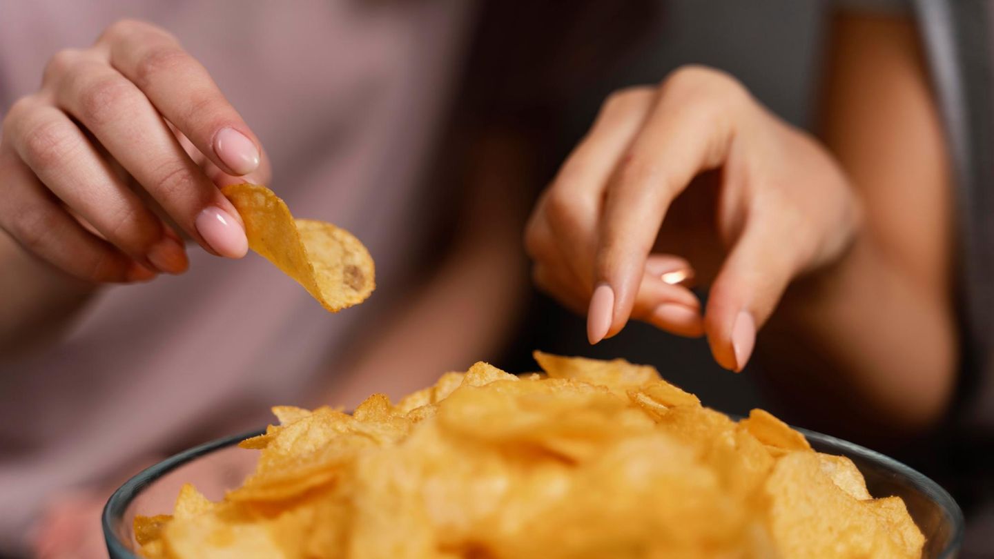 Eine weibliche Hand greift in eien Schale mit Chips