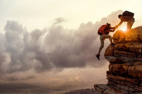 Zwei Menschen an einem Felsen, die einander helfen