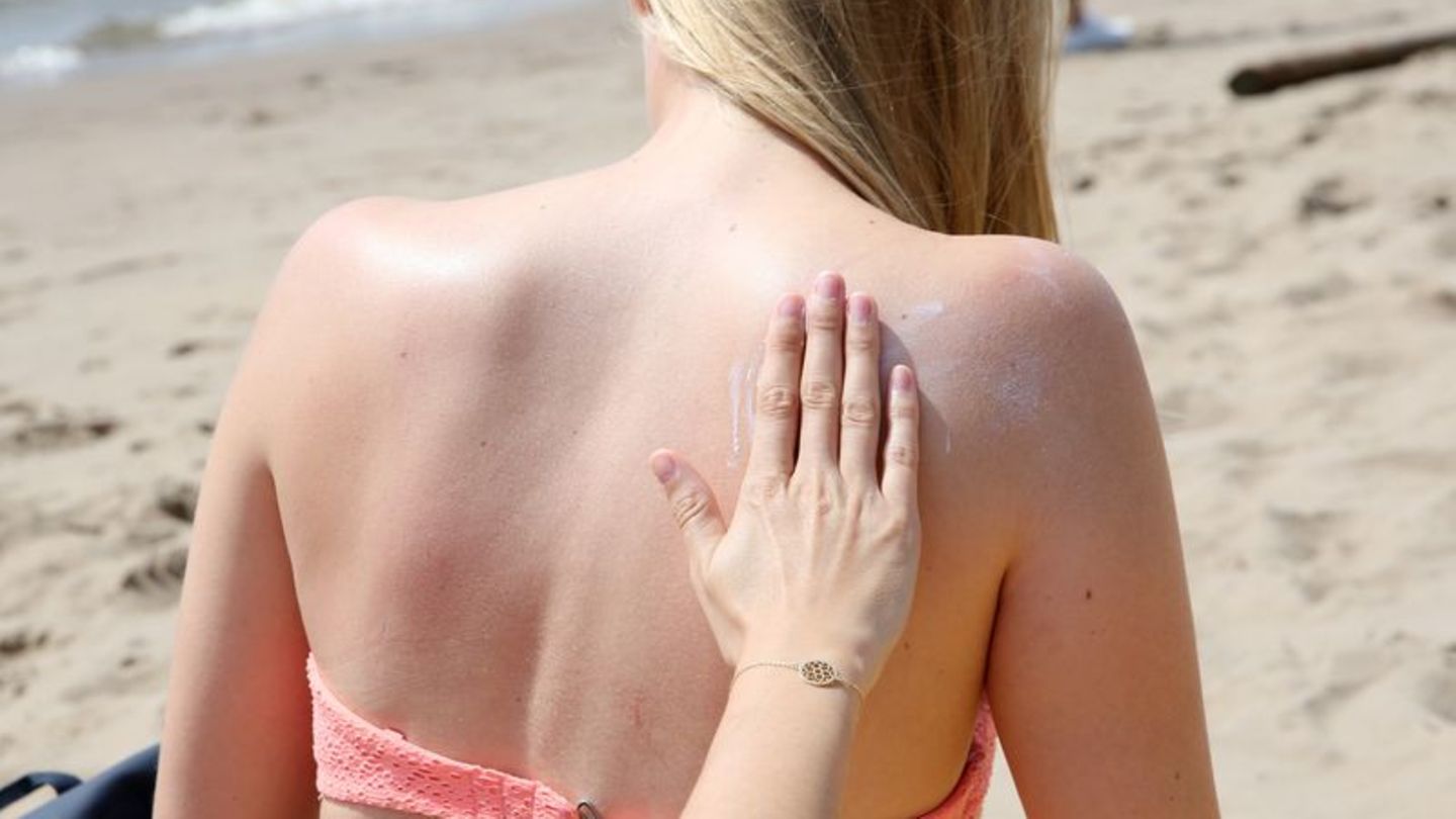 Eine Frau am Strand wird am Rücken eingecremt