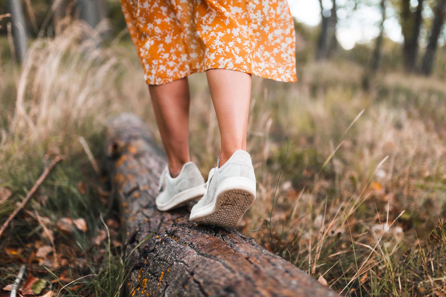 Eine Frau trägt nachhaltige Schuhe und balanciert auf einem Baumstamm.