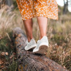 Eine Frau trägt nachhaltige Schuhe und balanciert auf einem Baumstamm.