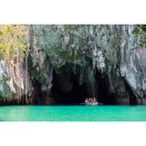 Ein kleines Boot mit mehreren Leuten am Eingang einer Höhle auf türkisfarbenem Wasser