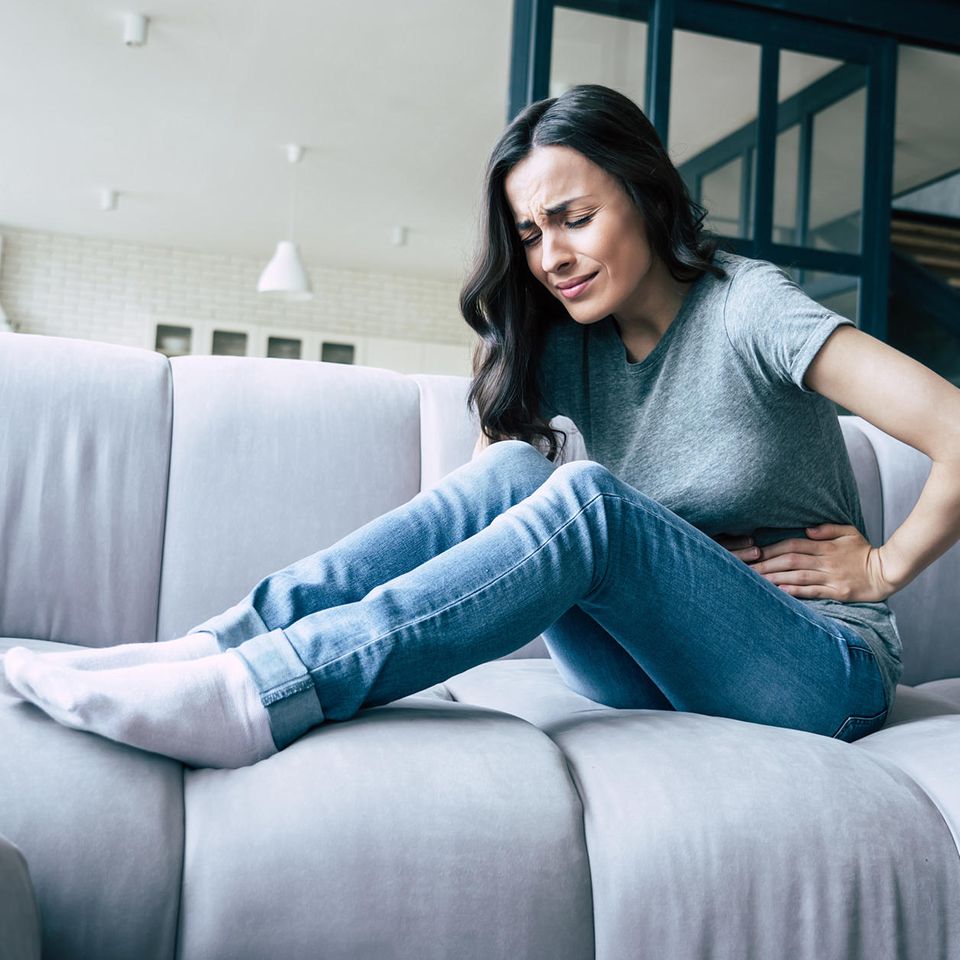 Eine Frau krümmt sich mit Bauchschmerzen