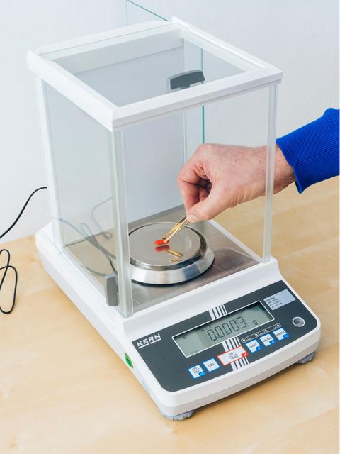 Eine rote Pille wird mit der Pinzette auf einer Waage platziert