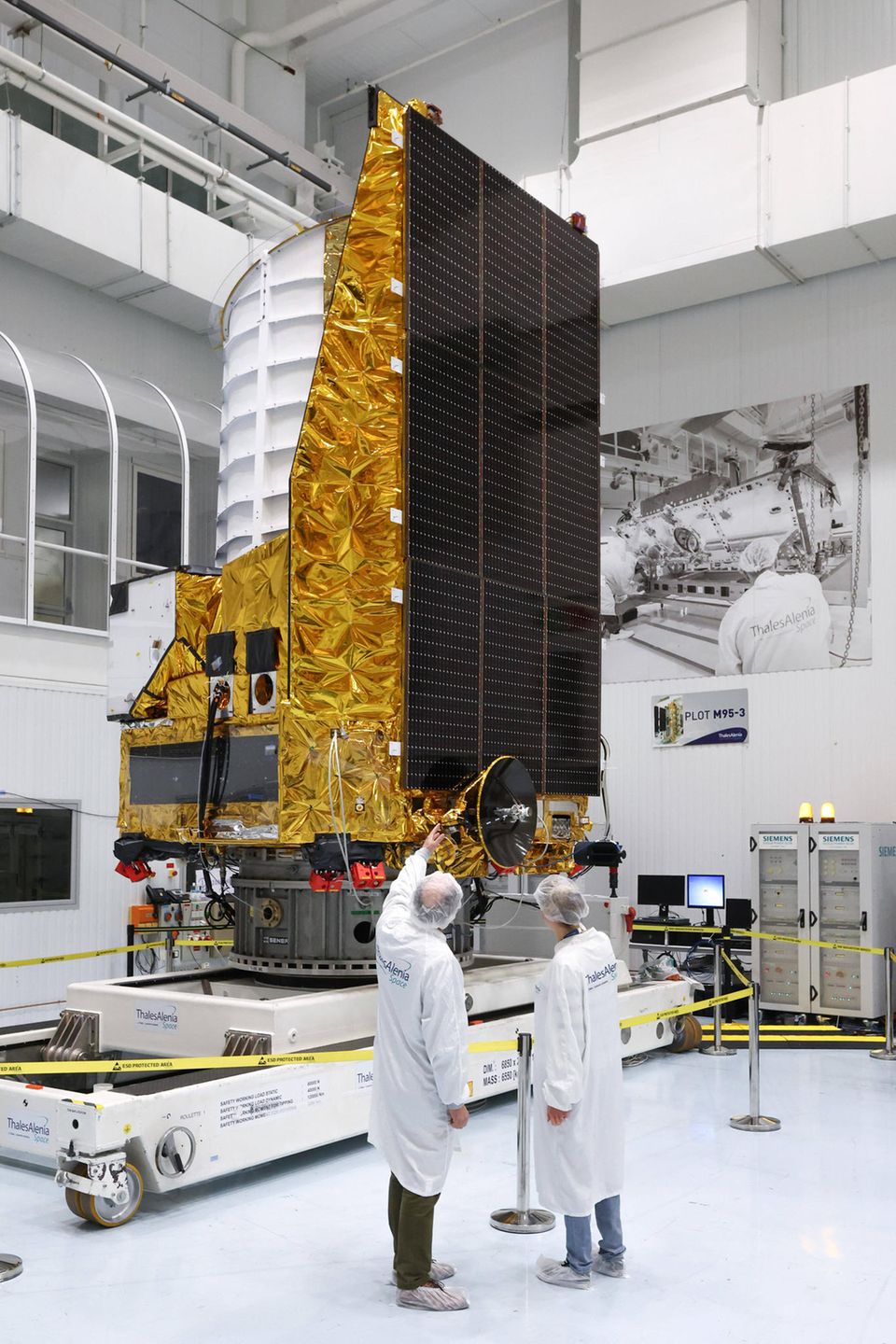 Zwei Menschen, von hinten zu sehen, stehen vor der Raumsonde Euclid, die sie um einige Meter überragt