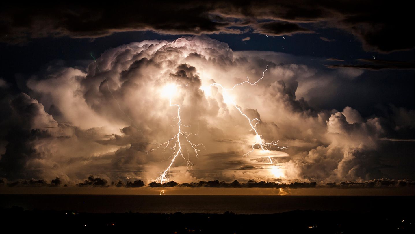 Große Gewitterwolke mit zwei herabzuckenden Blitzen über einer nächtlichen Bucht.