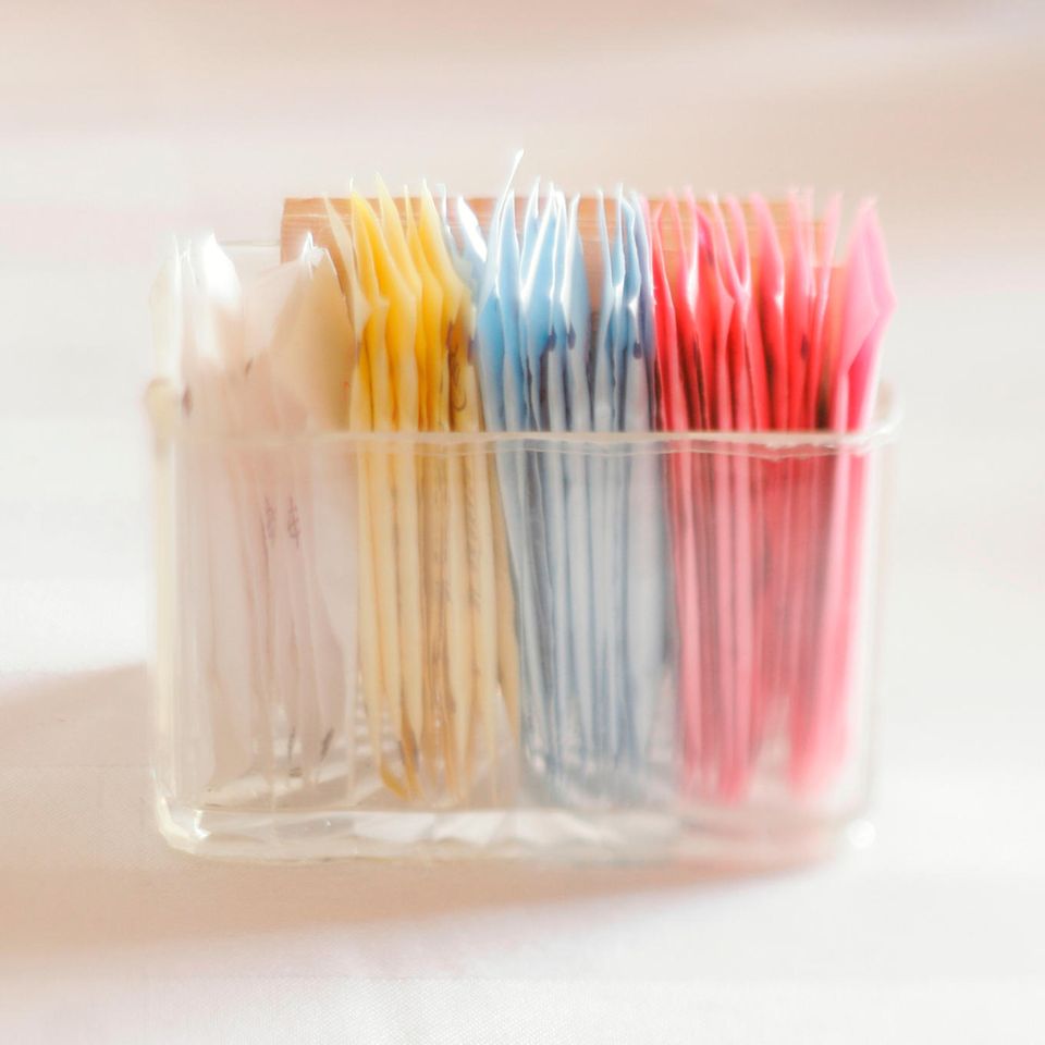 Bunte Packungen mit Süßstoffen in einem durchsichtigen Schälchen Bunte Packungen mit Süßstoffen in einem durchsichtigen Schälchen