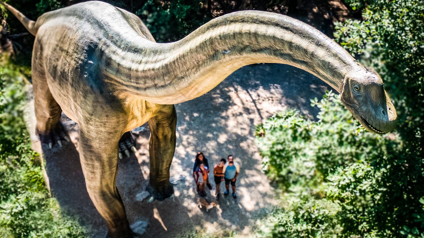Luftaufnahme: Ein riesiges Dinosauriermodell neben einer winzig wirkenden Gruppe von Menschen