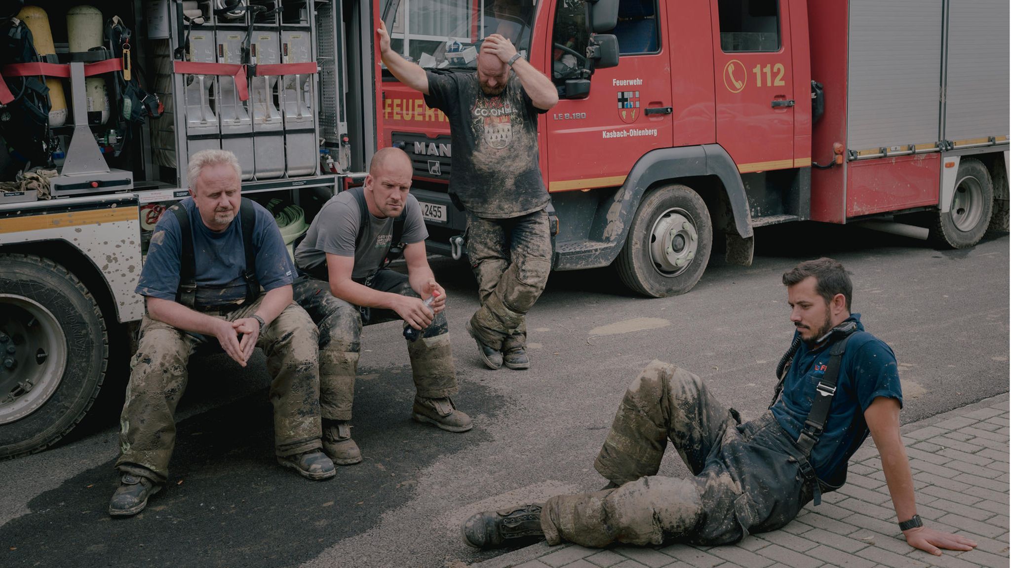Freiwillige Feuerwehrleute machen vor einem Feuerwehrauto eine Pause