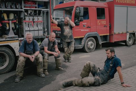 Freiwillige Feuerwehrleute machen vor einem Feuerwehrauto eine Pause