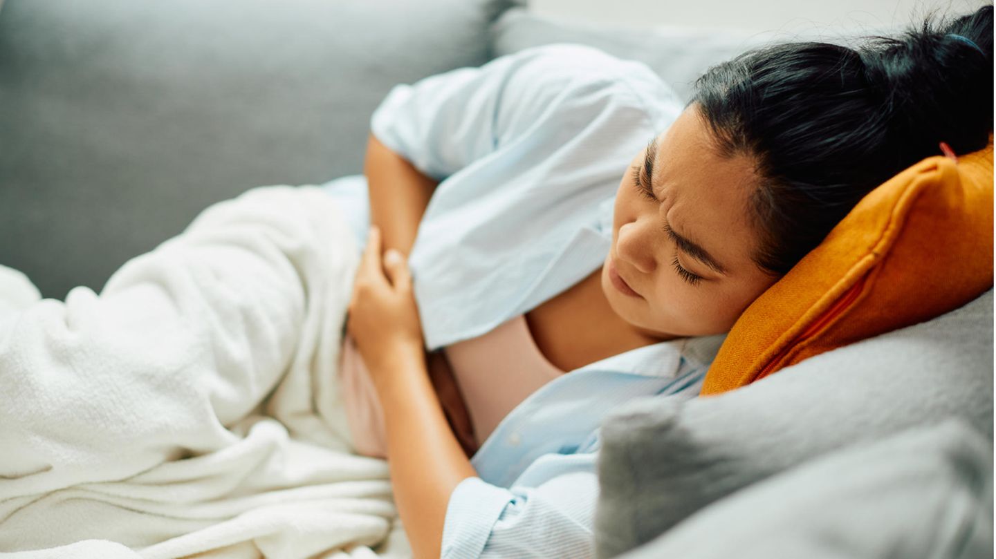 Frau liegt gekrümmt auf dem Sofa und hält sich den Bauch Frau liegt gekrümmt auf dem Sofa und hält sich den Bauch