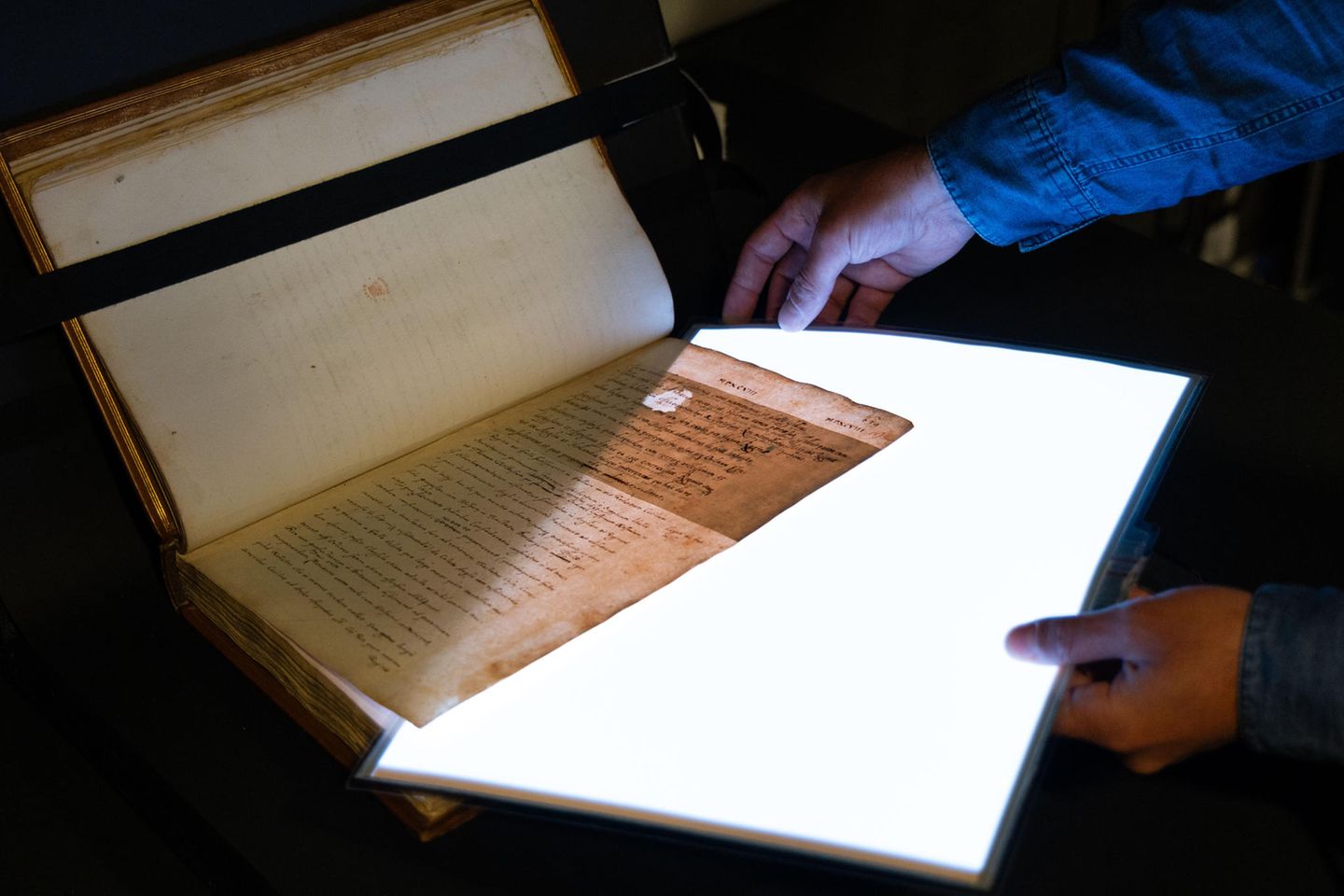 Seite eines alten Buchmanuskripts wird mithilfe einer starken Lichtquelle durchleuchtet