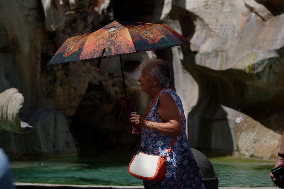 Eine alte Frau schützt sich in Rom mit einem Sonnenschirm und einem Getränk vor der Hitze