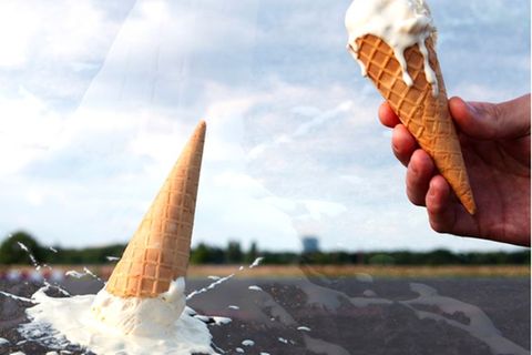 Eine Hand hält eine Eistüte während eine zweite Eistüte auf den Boden gefallen ist