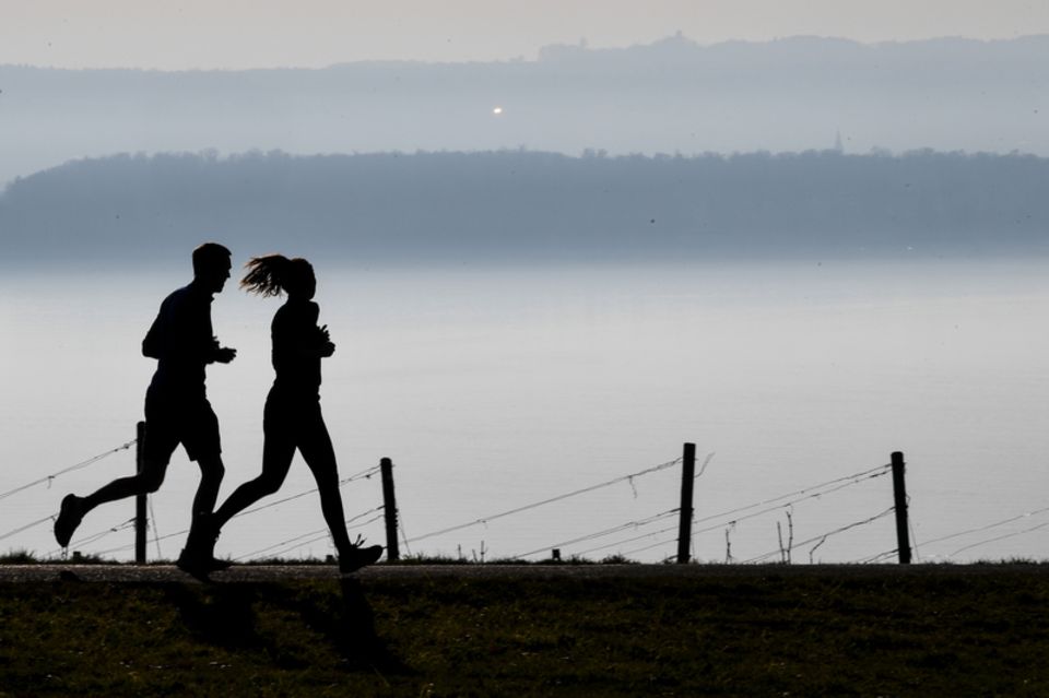 Mann und Frau joggen in der Dämmerung bei Nebel vor einer Bergkette  1.5009