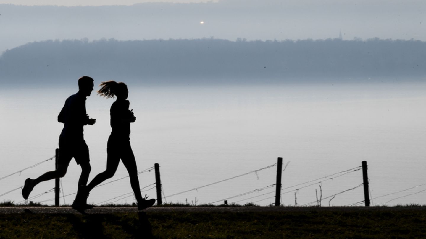 Mann und Frau joggen in der Dämmerung bei Nebel vor einer Bergkette