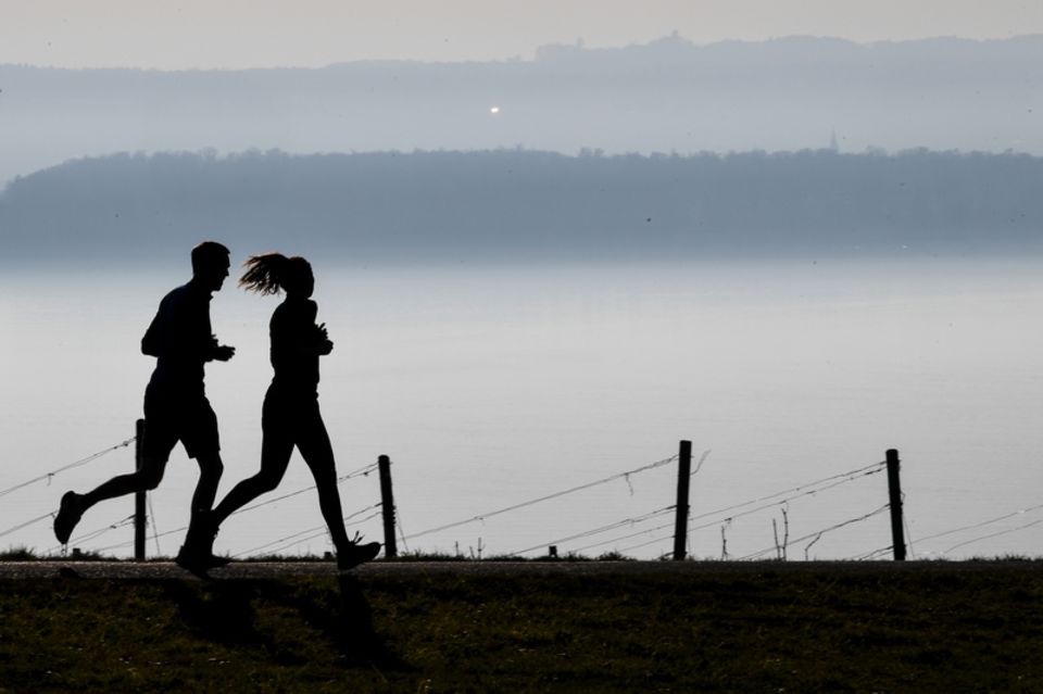 Mann und Frau joggen in der Dämmerung bei Nebel vor einer Bergkette
