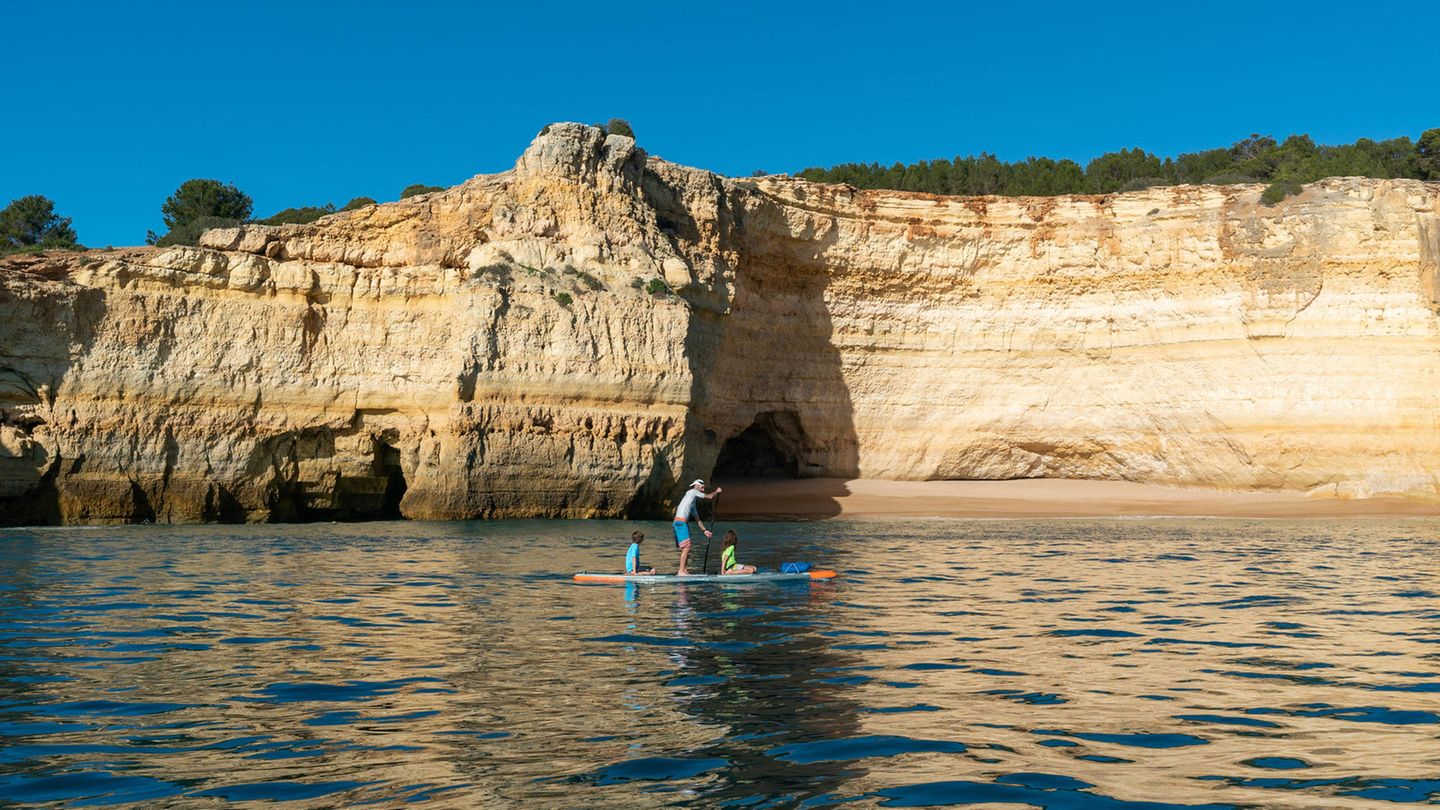 Ein Vater an der Algarve mit seinen Kindern im Meer auf einem SUP