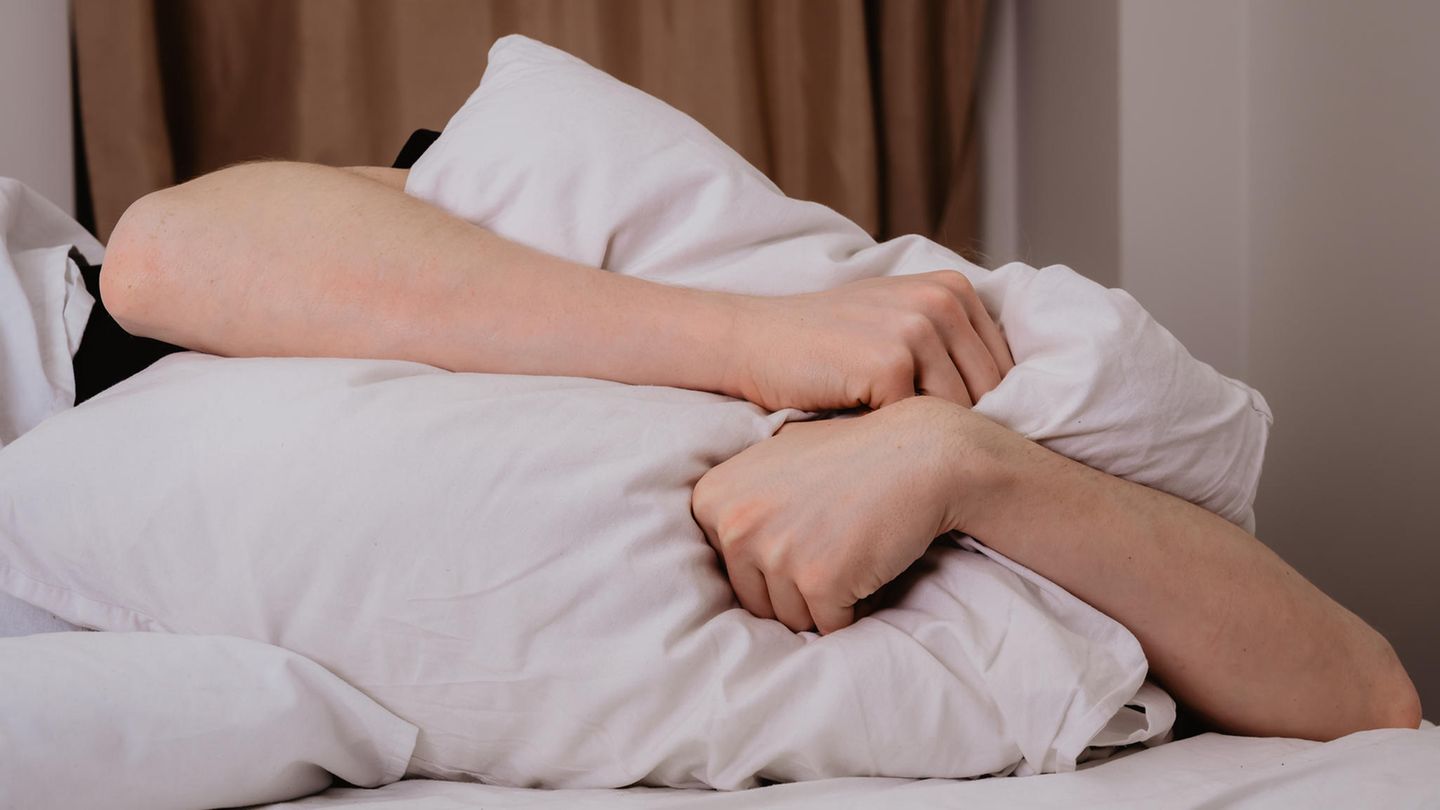 Ein Man drückt sich wegen Lärm sich das Kissen gegen den Kopf Ein Man drückt sich wegen Lärm sich das Kissen gegen den Kopf