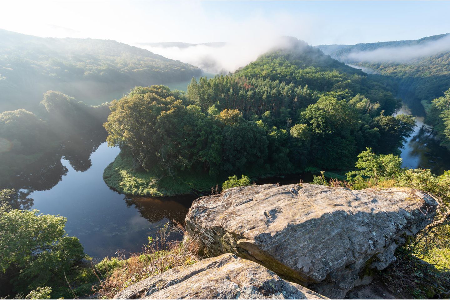 Panoramablick über einen sich windenden Fluss umgeben von Bäumen und tiefhängenden Wolken