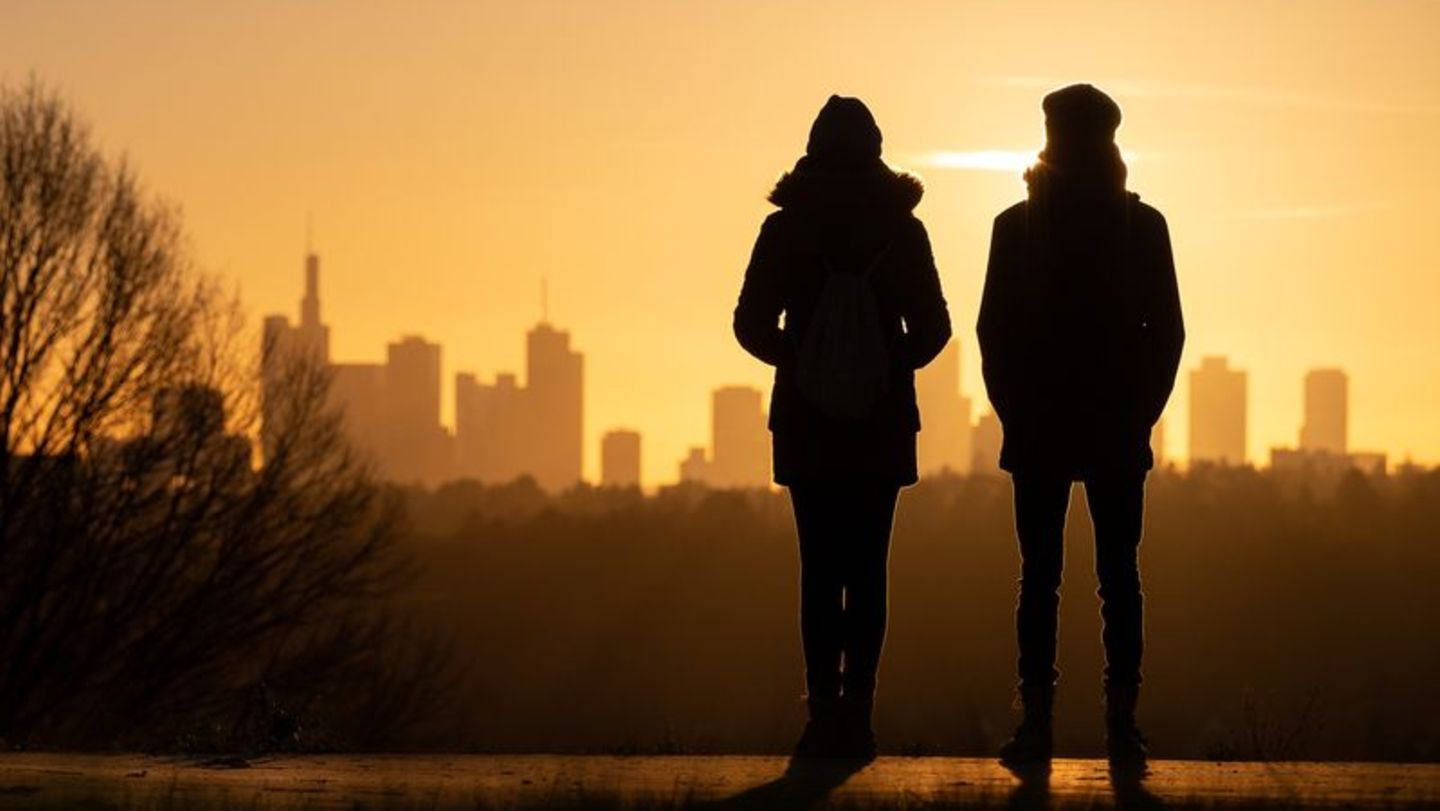 Frau und Mann blicken auf einen Sonnenuntergang vor einer urbanen Kulisse