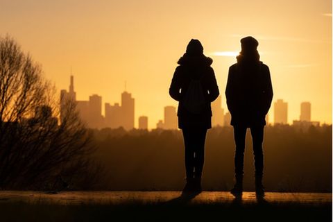 Frau und Mann blicken auf einen Sonnenuntergang vor einer urbanen Kulisse