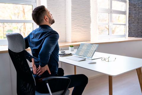 Mann sitzt mit Rückenschmerzen am Schreibtisch
