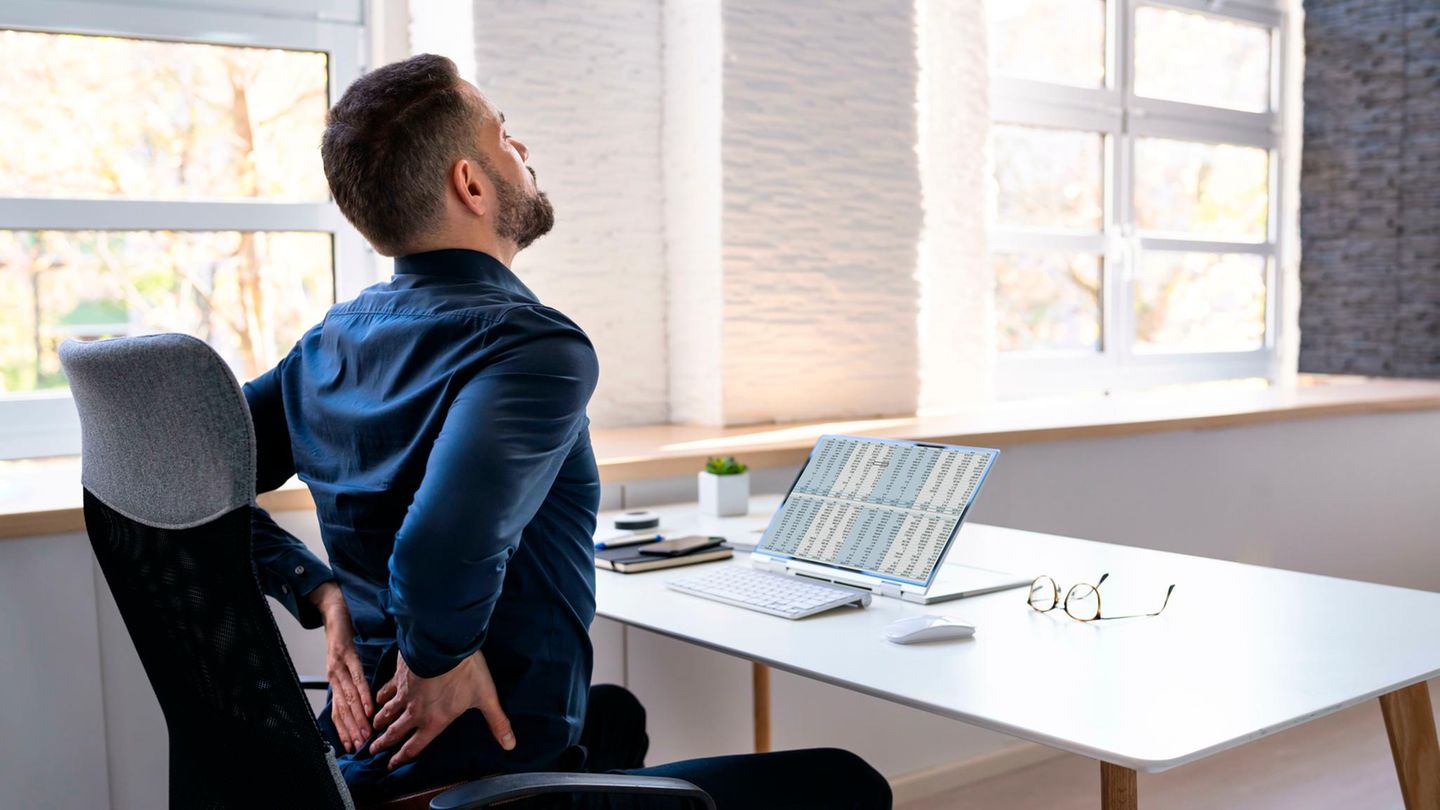 Mann sitzt mit Rückenschmerzen am Schreibtisch