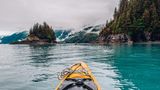 Zwei Kayaks unterwegs auf dem Wasser zwischen Bäumen und Bergen