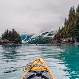 Zwei Kayaks unterwegs auf dem Wasser zwischen Bäumen und Bergen