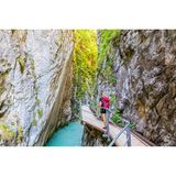 Eine Frau mit einem Rucksack läuft über einen schmalen Steg über hellblauem Wasser