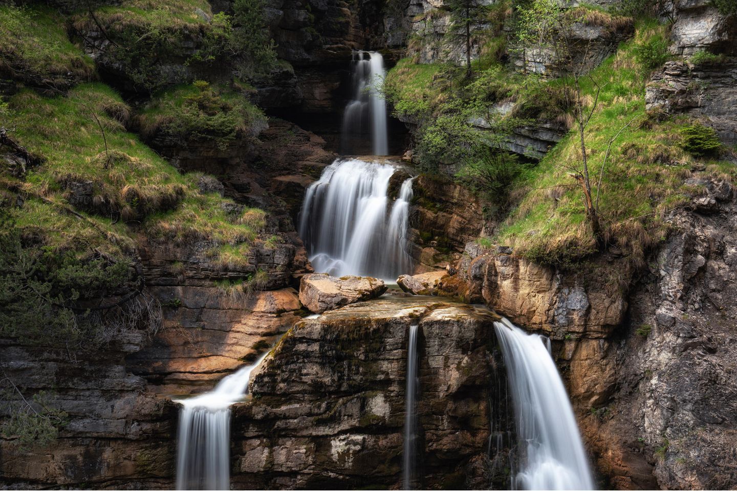 Blick auf einen Wasserfall, der in mehreren Stufen fällt und von Felsen und Pflanzen umgeben ist