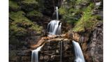 Blick auf einen Wasserfall, der in mehreren Stufen fällt und von Felsen und Pflanzen umgeben ist