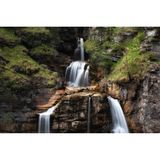 Blick auf einen Wasserfall, der in mehreren Stufen fällt und von Felsen und Pflanzen umgeben ist