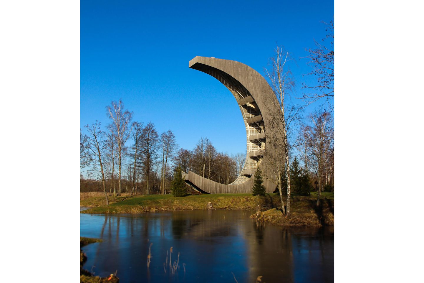 Der Holzturm hat die Form einer Mondsichel und steht direkt an einem See.