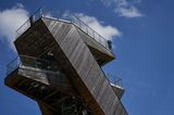 Der Turm ist aus Holz, die oberste Plattform schützt eine Reling aus Eisen. Der Himmel ist sommerlich weißblau.
