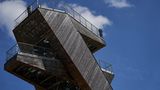 Der Turm ist aus Holz, die oberste Plattform schützt eine Reling aus Eisen. Der Himmel ist sommerlich weißblau.