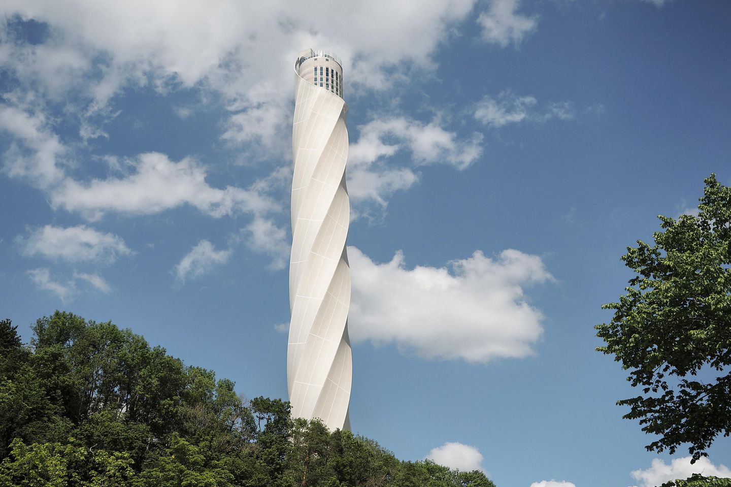 Versuchslabor: TK Elevator Testturm, Baden-Württemberg Der weiße Turm ragt in den wolkigen Himmel und erhebt sich über einen Wald.