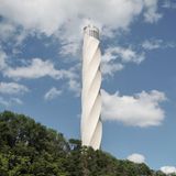 Der weiße Turm ragt in den wolkigen Himmel und erhebt sich über einen Wald.