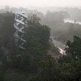 Im Nebel sieht man den Fluss Mur und ganz klein den hellen Turm, der an eine Doppelhelix erinnert.