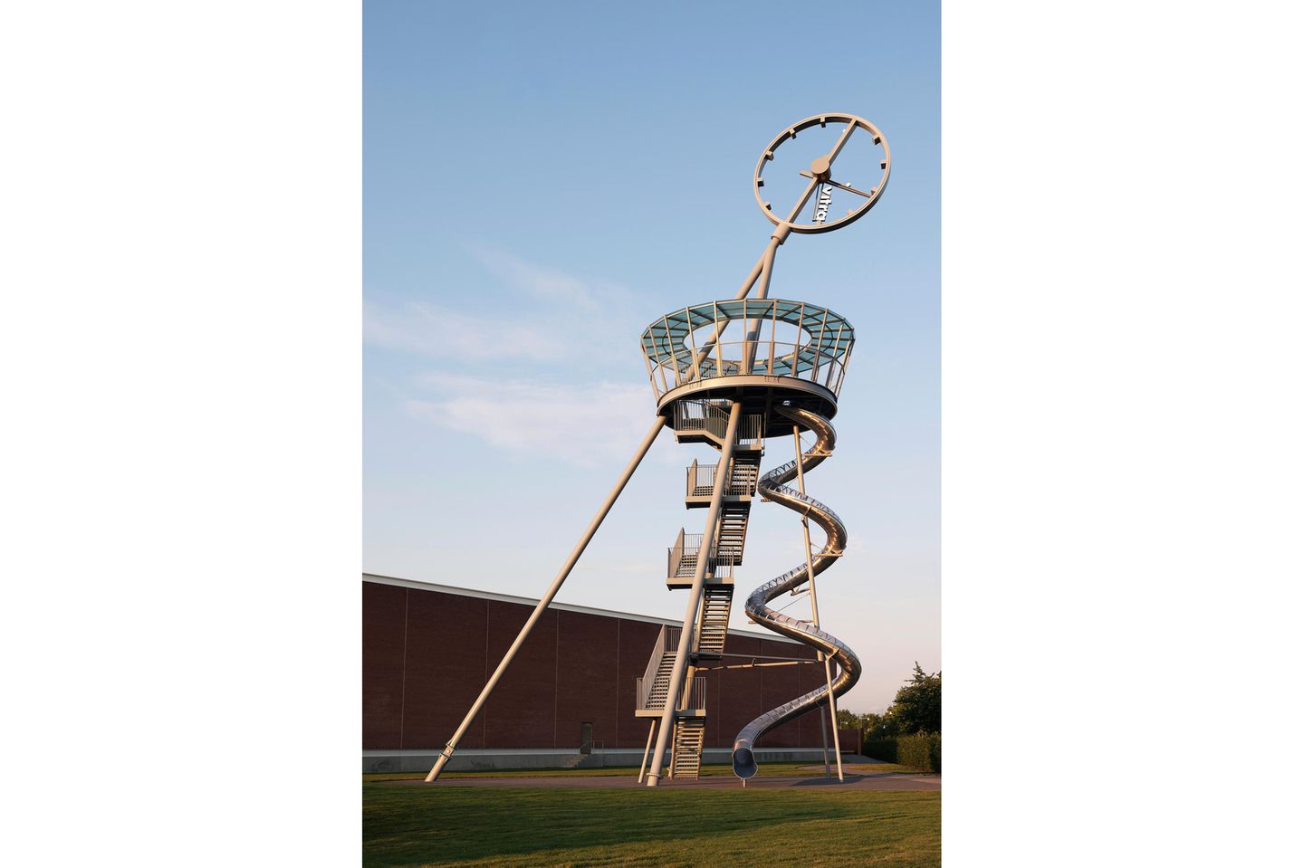 Schräglage: Vitra Slide Tower, Baden-Württemberg Der Turm ist schräg, ganz oben ist eine Uhr, neben der Treppe führt eine spindelförmige Rutsche nach unten.