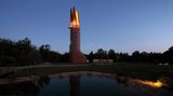 Leuchtfeuer: Regionalparkturm, Hessen Der Turm steht in einer Abendstimmung am Waldrand, seine Spitze besteht aus vier Teilen, die beleuchtet sind.