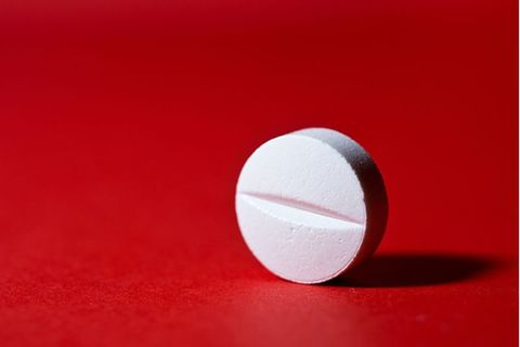Weiße Tablette mit einer Einkerbung in der Mitte vor rotem Hintergrund