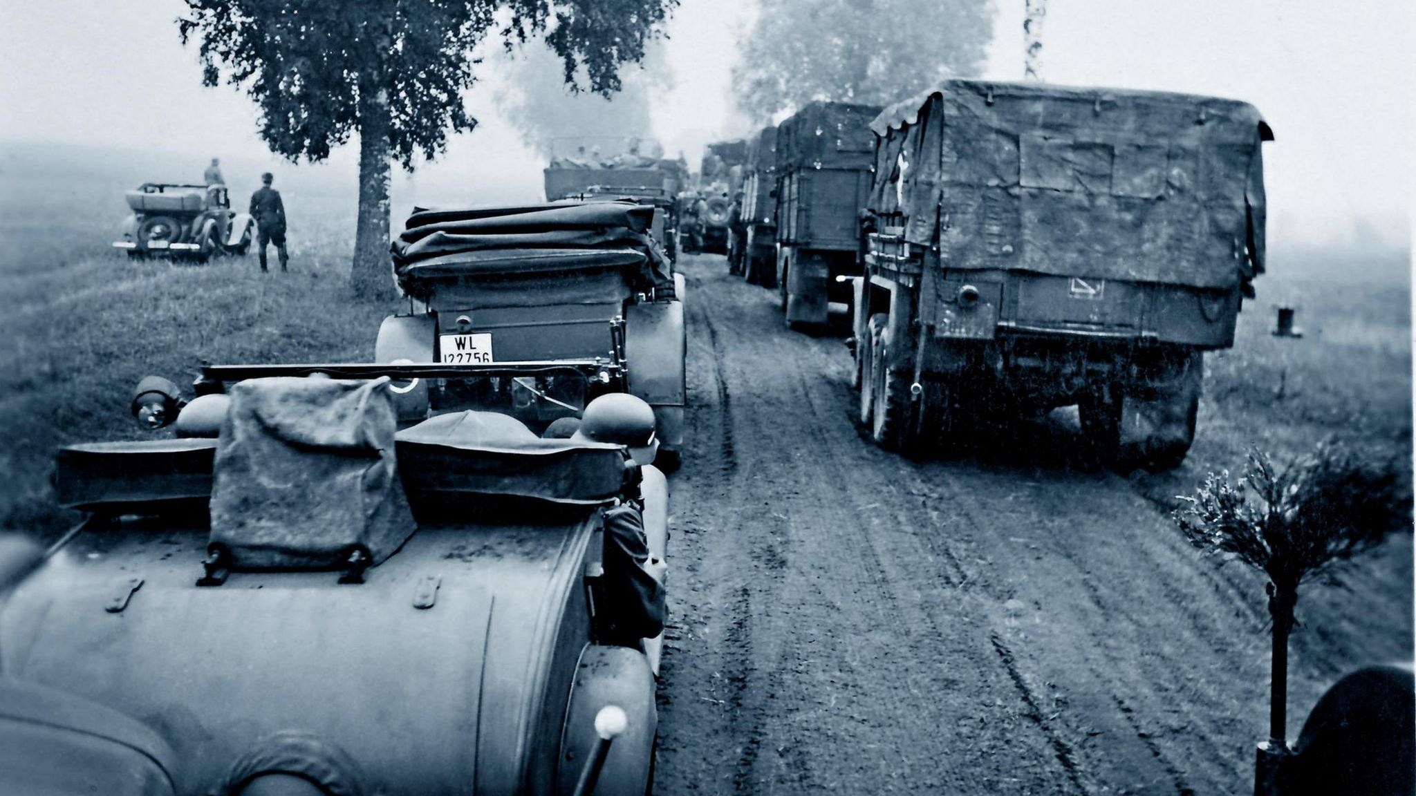 Deutsche Soldaten fahren in Autos und Militärlastern eine Feldstraße entlang